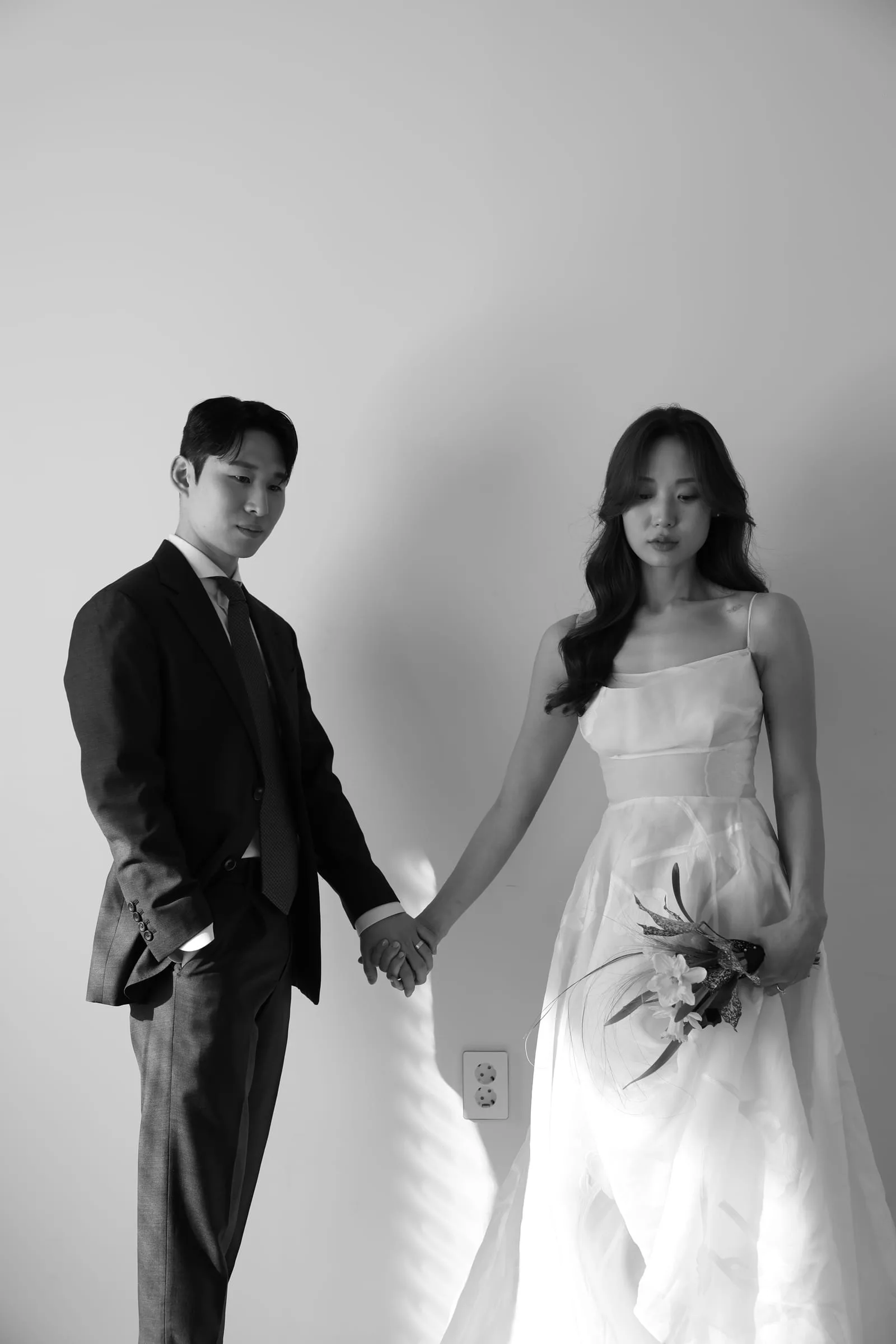 흑백 스튜디오 — 어두운 예복의 신랑과 웨딩드레스 신부가 손을 맞잡은 결혼 사진