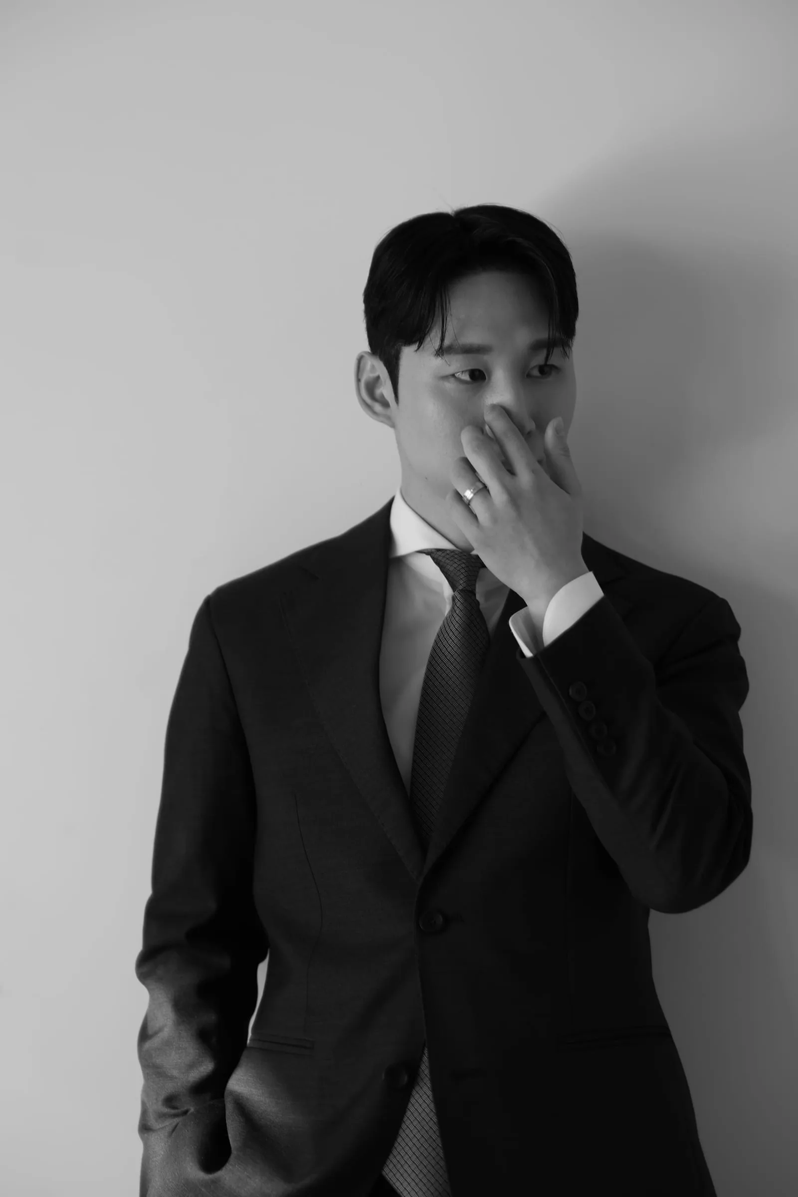 흑백 포트레이트 — 어두운 수트와 타이를 맨 신랑이 생각에 잠긴 채 한손으로 얼굴을 살짝 가린 모습