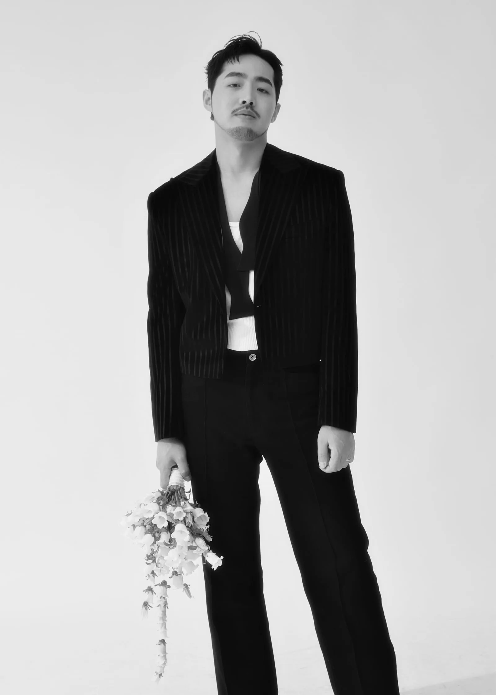 흑백 전신 — 핀스트라이프 블랙 수트에 케스케이드 꽃다발을 손에 들고 선 신랑