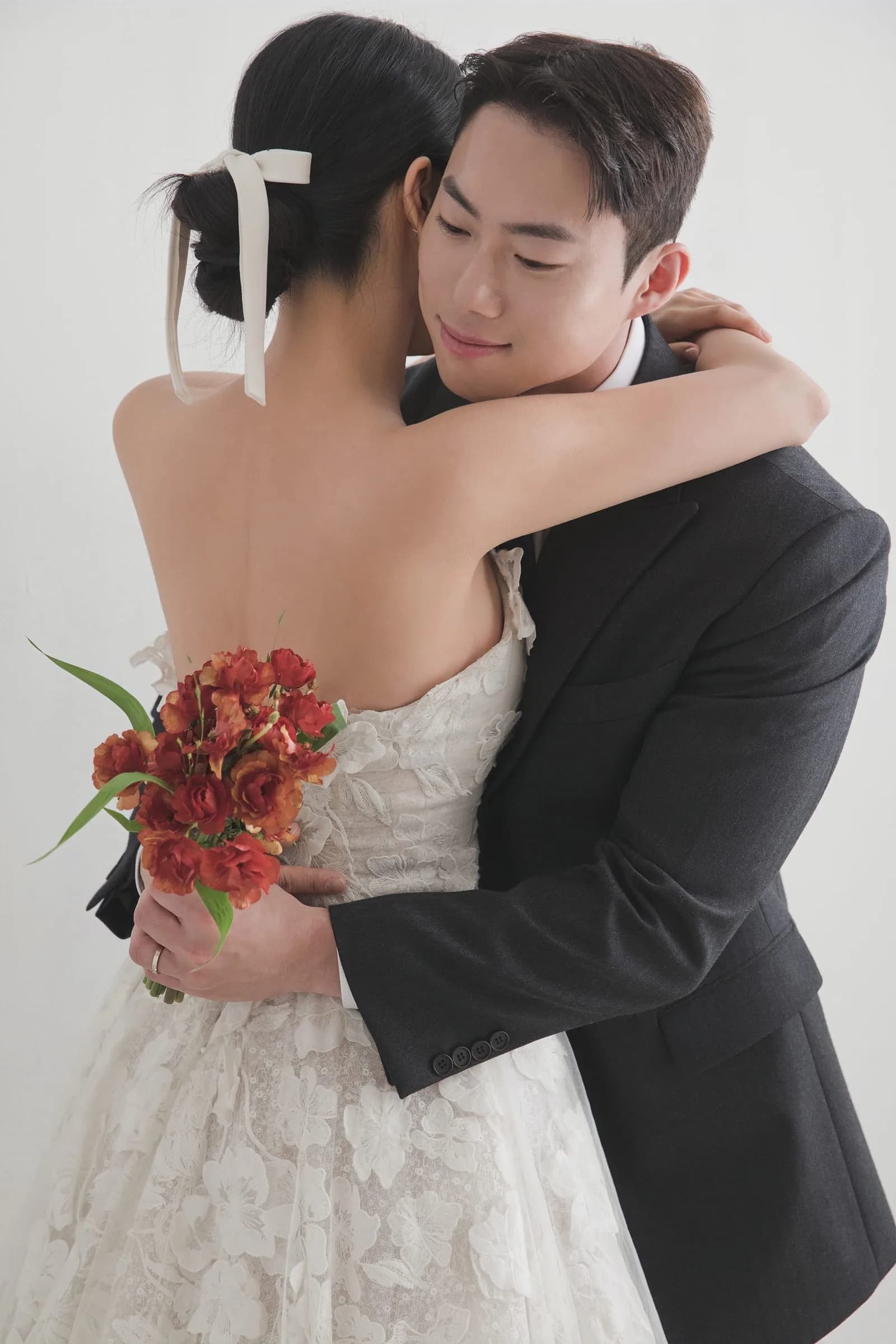 컬러 — 차콜 예복 수트 신랑이 붉은 꽃다발 든 신부를 다정하게 안고 있는 웨딩 스튜디오 사진